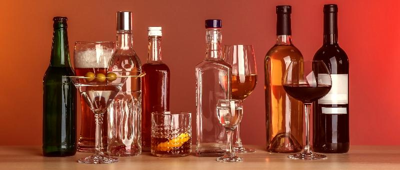 Table with different bottles of wine and spirits on color background